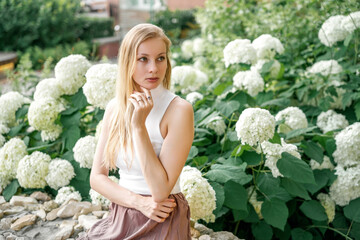 beautiful blonde woman is sitting in a city park with hydrangeas