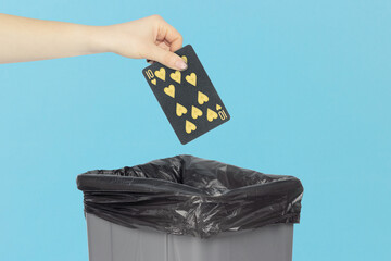Throwing black playing card hearts 10 into the trash can, outstretched hand with playing card in front of trash can