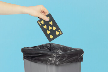 Throwing black playing card hearts 9 into the trash can, outstretched hand with playing card in front of trash can