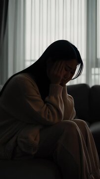 Silhouette of a stressed woman suffering from a severe migraine and holding her head in a dark moody living room, illustrating mental health burnout concepts.