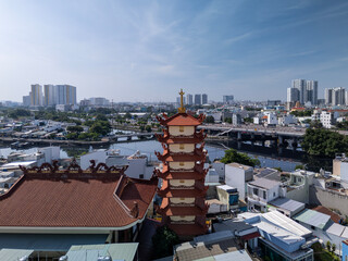 Drone view over Buddhist temple in busy urban area of Ho Chi Minh City, Vietnam on a sunny clear day featuring roof decoration and the transportation infrastructure of main roads and canals

