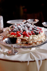 Festive, multi-layer cake layered with cream and topped with powdered sugar and fresh berries. Presented on a silver cake stand, ready for celebration, party, or family gathering.