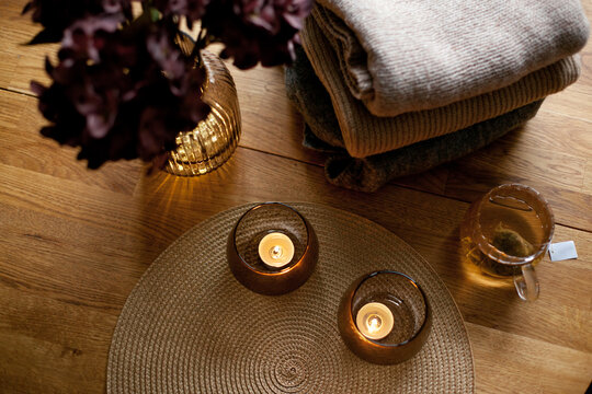 Home interior decor in brown colors: glass vase with dried flowers, candles and cup of warm tea