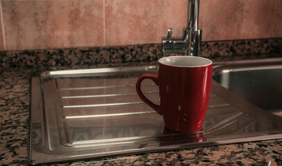 Red coffee mug resting on kitchen sink. Mockup template