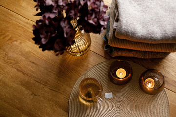 Home interior decor in brown colors: glass vase with dried flowers, candles and cup of warm tea