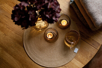 Home interior decor in brown colors: glass vase with dried flowers, candles and cup of warm tea