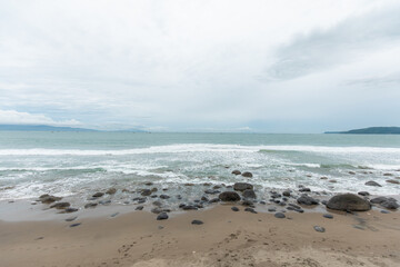 Overcast day on a rough, rocky tropical beach with incoming ocean waves and wet stones