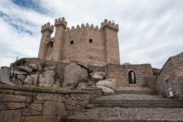 Castelo de Penedono, uma imponente fortifica&ccedil;&atilde;o medieval, com a sua torre principal e ameias piramidais destacadas contra um c&eacute;u carregado de nuvens em Portugal