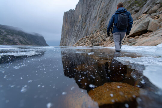 A figure traverses the icy shoreline bordered by towering cliffs, illustrating the raw beauty of nature and the adventurous spirit of exploration in challenging environments.