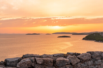 An orange sunset over the sea with many islands in the water, a coastal landscape from a hilltop...
