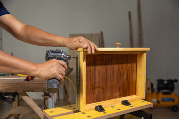 Man's hand using impact screwdriver to fasten drawer slide rail to wooden cabinet.