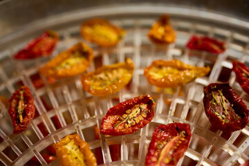Bright red and yellow cherry tomatoes are arranged in a dehydrator, drying under warm air. This healthy method preserves their flavor, perfect for summer snacks.