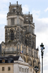 Fototapeta premium Gothic Orleans Cathedral towers rising behind Hotel de Ville building facade. Historic French architecture landmark in Loiret region with flag on roof against cloudy blue sky on a sunny day
