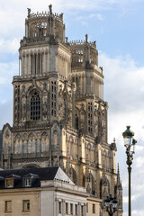 Fototapeta premium Gothic Orleans Cathedral towers rising behind Hotel de Ville building facade. Historic French architecture landmark in Loiret region with flag on roof against cloudy blue sky on a sunny day