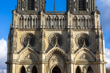 Facade of Sainte Croix Cathedral in Orleans, France. Gothic architecture with twin towers, rose windows and stone statues. Historic religious building exterior on a sunny day against blue sky.