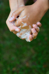 Two hands are rubbing together with soap bubbles while standing outdoors in a green garden. This activity showcases the importance of hygiene and cleanliness.