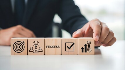 Businessperson arranging wooden blocks with business process symbols on a white desk, representing strategy and success in a corporate setting.