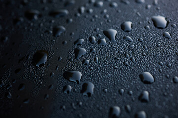 Water droplets glisten on a smooth, dark surface in soft light. This scene captures the beauty of morning dew resting on an object, showcasing natural patterns.