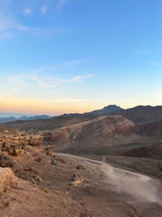 Panorama of desert at sunset: dusty road, hills and pink-yellow horizon