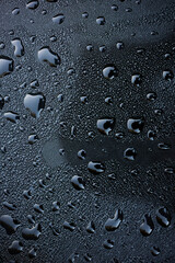 Water droplets glisten on a smooth, dark surface in soft light. This scene captures the beauty of morning dew resting on an object, showcasing natural patterns.
