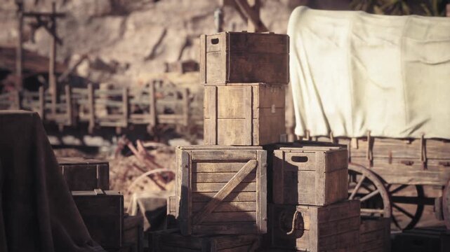A collection of rustic wooden crates is stacked in an outdoor area, surrounded by old carts and nature, capturing a vintage, historical atmosphere during the day.