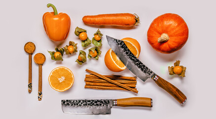 A pumkin, orange pepper belle, physalis fruits and a carrot with knives on white background