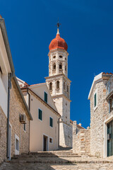 Fototapeta premium The Catholic Church of St. Francis with a high tower in the town of Betina in Croatia, stone buildings in a narrow alley, a sunny summer day.