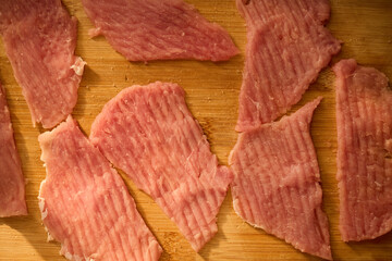 Thin slices of raw meat lay on a wooden cutting board, ready for cooking. The kitchen has warm lighting, creating a cozy atmosphere for meal preparation.