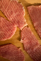 Thin slices of raw meat lay on a wooden cutting board, ready for cooking. The kitchen has warm lighting, creating a cozy atmosphere for meal preparation.