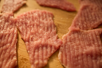 Thin slices of raw meat lay on a wooden cutting board, ready for cooking. The kitchen has warm lighting, creating a cozy atmosphere for meal preparation.