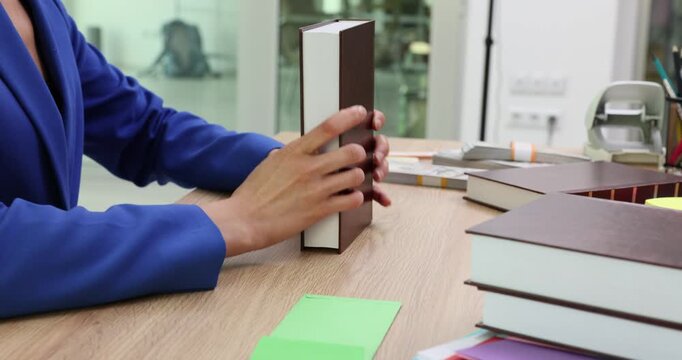 Woman office worker reviews books and stacks in pile on table. Businesswoman examines contents of books and stacks neatly to keep workspace clear