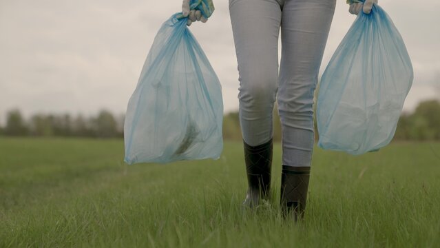 A man carries garbage in garbage bags on green grass, collection and disposal of unnecessary waste, a woman in gloves for cleaning work, help protecting the planet's environment, clean earth.
