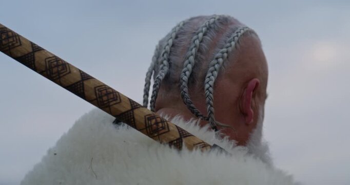 Viking warrior with axe standing on mountain cliff, wearing fur cloak and leather armor, overlooking dramatic landscape. Historical Nordic fighter, strength and adventure concept. Slow motion