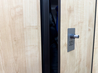 Open gym locker door with personal belongings. Wooden door features modern closing mechanism and personal locker number. Concept for storing belongings while working out at gym