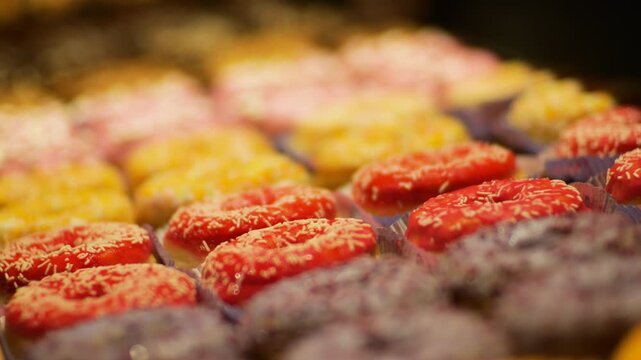 A close-up of delicious donuts with colorful icing. The camera focus slowly pans down the row of sweet pastries. These mouth-watering shots are perfect for food-related projects.