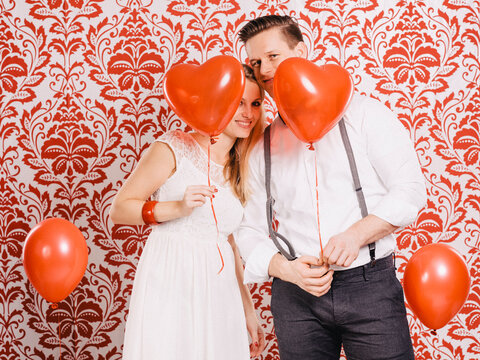 Junge Frau und junger Mann mit roten Herzballons vor roter Tapetenwand