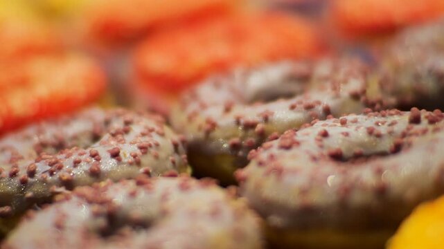 A close-up of delicious donuts with colorful icing. The camera focus slowly pans down the row of sweet pastries. These mouth-watering shots are perfect for food-related projects.