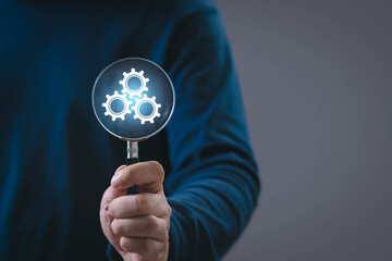 A person holding a magnifying glass highlighting glowing gear icons, symbolizing process optimization, technical analysis, system improvement, productivity enhancement, and modern business solutions.