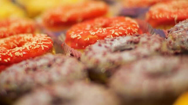 A close-up of delicious donuts with colorful icing. The camera focus slowly pans down the row of sweet pastries. These mouth-watering shots are perfect for food-related projects.