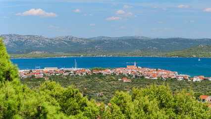 The coastal town of Murter in Croatia is situated on the seashore with a mountainous landscape,...
