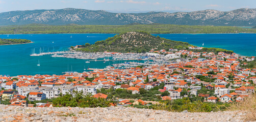 Fototapeta premium The coastal town of Murter in Croatia is situated on the seashore with a mountain landscape, seen from the top of Mount Raduc on a sunny summer day.