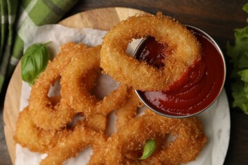 Deep fried squid rings with basil and ketchup on wooden table, flat lay