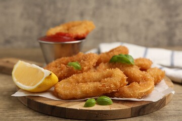 Deep fried squid rings with lemon slice, basil and ketchup on wooden table, closeup