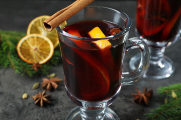 Tasty mulled wine in glass mugs, spices and fir branches on grey table, closeup