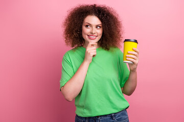 Young woman wearing a bright green tshirt holds a yellow coffee cup and smiles against a pink background advertising fashion lifestyle