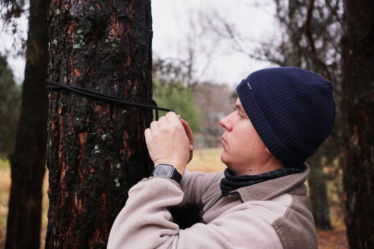 a young man ties a rope to a tree using a knot. The concept of camping and outdoor recreation