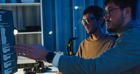 Team adult male engineer collaborate on robotic hand project using AI code solutions machine learning at tech workspace night. Artificial intelligence interface, collaboration prototype development.