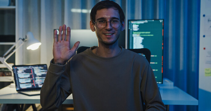 Adult male freelance programmer work late speak in online meeting video conference and looking at camera in tech office night. Artificial intelligence, robotics, user interface, machine learning.