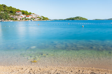 The seaside town of Tisno in Croatia is situated on the shores of a blue sea with many hills, the landscape on a sunny summer day, view from the beach.
