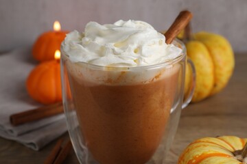Delicious pumpkin latte with whipped cream in glass cup, cinnamon sticks, fresh vegetables and burning candles on table against grey background, closeup